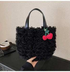 Dettaglio borsa in peluche nera con manico in pelle e ciondolo a forma di ciliegia rossa