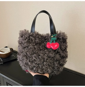 Dettaglio borsa in peluche grigio con manico in pelle nera e ciondolo a ciliegia