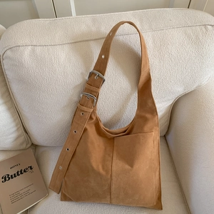 Brown faux suede hobo shoulder bag with wide strap and retro metal buckles on sofa