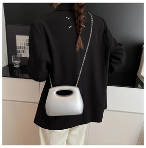 Silver acrylic mini clutch bag shown with chain strap on model in a minimalist setting