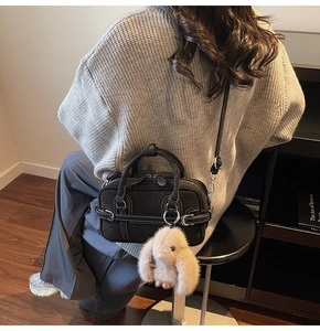 Detail of black Boston bag with white stitching and cute long-eared rabbit plush charm