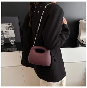 Detail of dark burgundy handbag with hollow handle and gold chain on a model