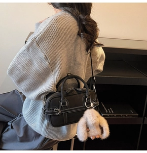 Detail of black vintage shoulder bag with white contrast stitching and plush rabbit charm