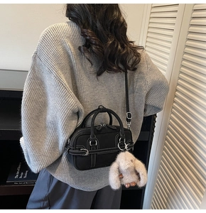 Detail of a black Boston bag with white stitching and a plush rabbit pendant in a room