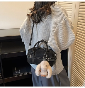 Detail of black suede crossbody bag with white stitching and plush bunny charm