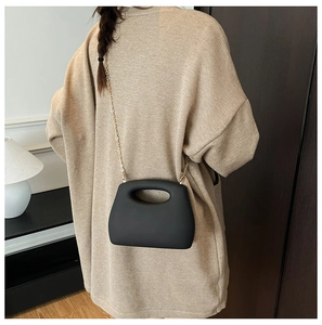 Model wearing a black matte geometric crossbody bag with a gold chain and cutout handle