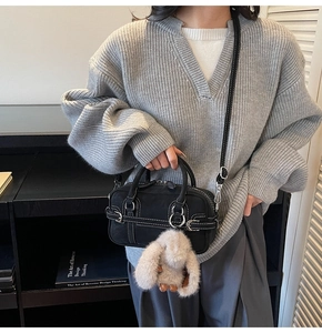 Detailed view of a black canvas bag with white contrast stitching and a plush rabbit charm