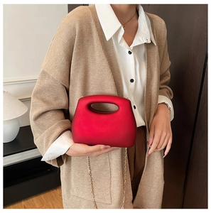 Detail of red matte acrylic clutch bag with hollow handle and gold chain strap on model