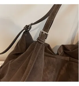Detail of silver buckle and white contrast stitching on a brown suede tote bag shoulder strap