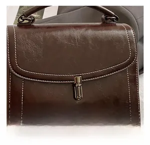 Detail of silver twist lock and white contrast stitching on a vintage brown leather bag