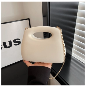 Detail of cream acrylic clutch bag with oval cutout handle and gold chain strap