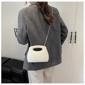 White structured acrylic evening bag with gold chain strap shown on person in a modern interior