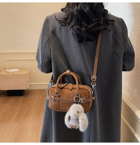 Brown retro mini Boston bag with white bunny charm shown on model in stylish interior