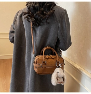 Detail of brown vintage baguette bag with white stitching and plush rabbit charm
