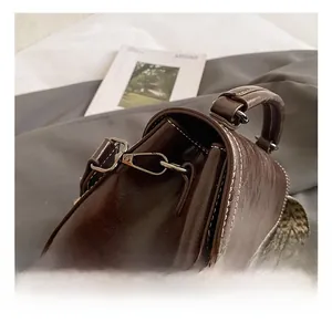 Close-up of silver metal hook and contrast stitching on dark brown leather handbag