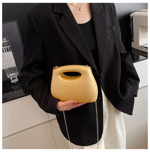 Detail of yellow acrylic evening clutch bag with chain strap and cutout handle on model