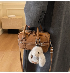 Close-up of brown suede Boston bag with plush white rabbit charm and silver metal hardware