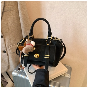 Detail of vintage black messenger bag with gold twist lock and pony charm on a suitcase
