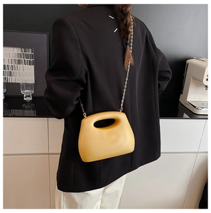 Detail of a bright yellow acrylic box bag with a circular cutout handle and gold chain strap