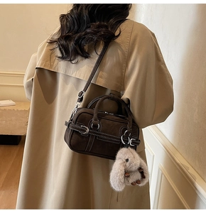 Detail of dark brown suede shoulder bag with contrast stitching and rabbit charm