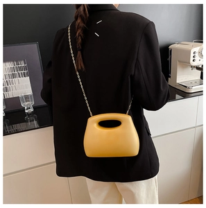 Detail of a bright yellow acrylic evening bag with a gold chain strap on a model