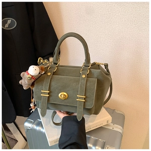 Detailed view of dark green matte shoulder bag with gold twist lock and plush monkey charm