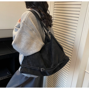 Detail of black suede tote bag with contrast stitching and adjustable buckle on shoulder strap