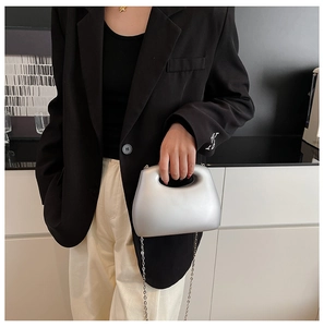 Model wearing silver metallic acrylic clutch bag with chain strap in modern interior