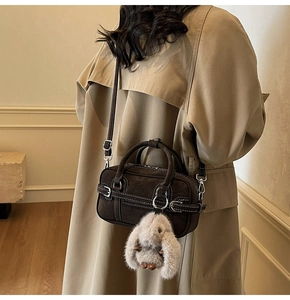 Detail of dark brown suede shoulder bag with white contrast stitching and plush rabbit charm