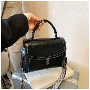 Detail of black leather handbag with white stitching and ethnic patterned wide strap