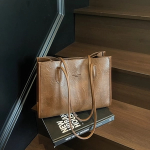Vintage brown PU leather tote bag with long straps on dark wooden stairs