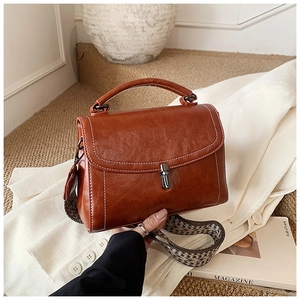 Close-up of brown vintage handbag with patterned wide strap on white blazer background