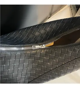 Close-up of smooth silver metal zipper on black woven leather tote bag texture
