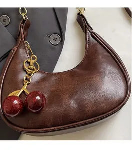 Close-up of brown crescent bag with retro texture and sequined cherry charm accessory
