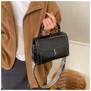 Close-up of black crossbody bag with white contrast stitching and woven shoulder strap