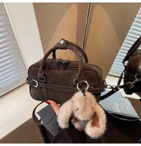 Detail of dark brown vintage Boston bag with white stitching and plush rabbit charm