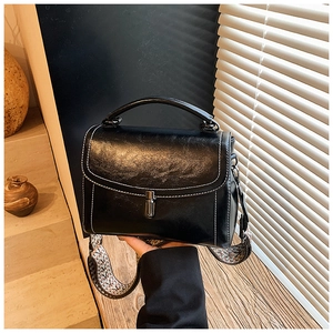 Detail of black leather handbag featuring white contrast stitching and a woven strap