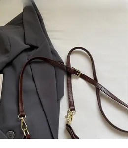 Detail of adjustable brown leather shoulder strap with gold buckle on gray fabric