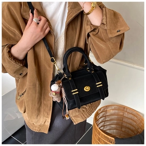 Detail of a black matte messenger bag with a golden turn-lock and brown teddy charm