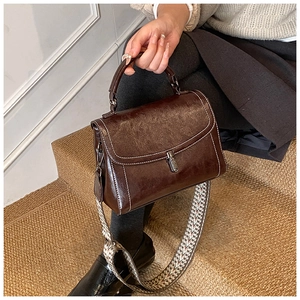 Detail of vintage brown crossbody bag with white stitching and woven geometric strap