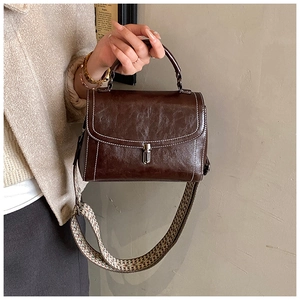 Detail of vintage brown leather handbag with contrast stitching and woven shoulder strap