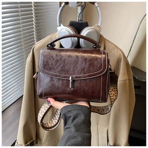 Detailed shot of dark caramel brown leather bag with retro buckle and colorful woven strap