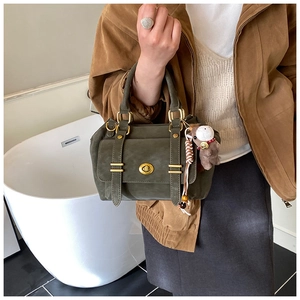 Close-up of green matte messenger bag with gold turn-lock and teddy bear charm