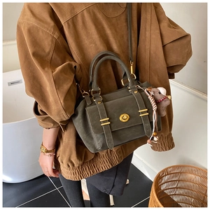 Detail of dark green messenger bag featuring a hippo plush pendant and golden twist lock
