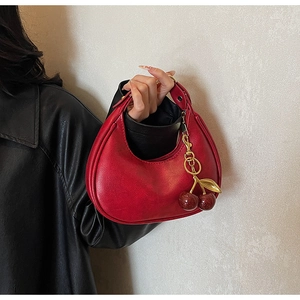Detail of red crescent hobo bag with a metallic cherry charm and smooth leather texture