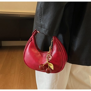 Detail shot of a red leather crescent bag featuring a delicate cherry charm and gold leaf