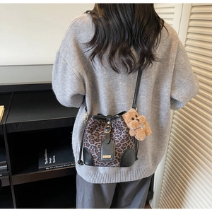 Detail of leopard print bucket bag featuring leather trim and a cute plush bear charm