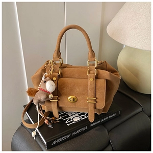 Detail of vintage brown suede messenger bag with gold hardware and horse charm on a book