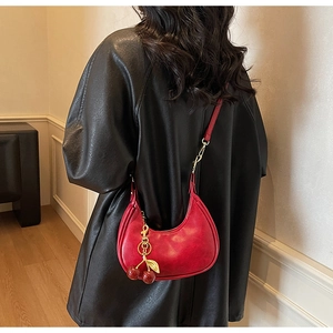 Detail of red crescent hobo bag with gold metal cherry pendant on black leather jacket