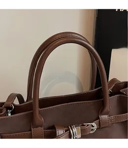 Detail of soft matte leather handle with metallic buckle on a brown tote bag